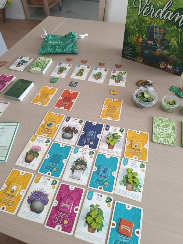 Wide view of a Verdant game in progress with the market, cloth bag, tokens and a growing plant and room tableau on the table