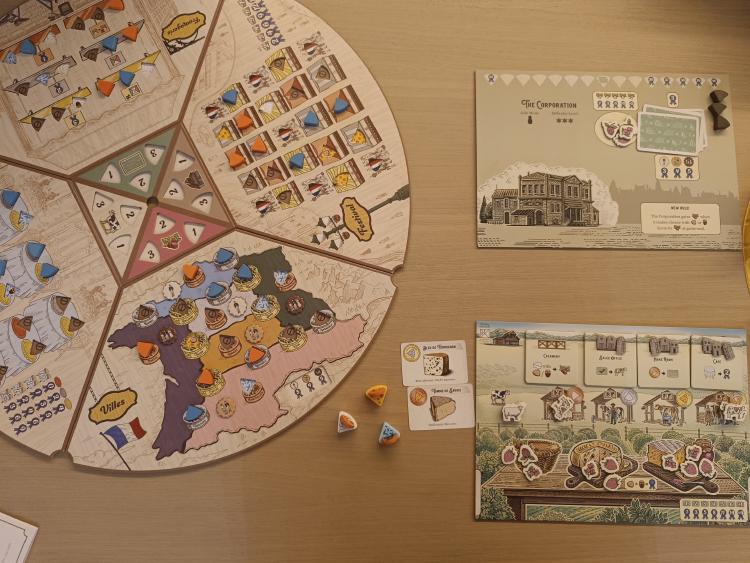 Overhead view of a completed Fromage board next to the Corporation solo mode board, cheese tokens and cards scattered nearby