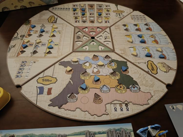 Fromage game board mid-play showing all four venue quadrants with cheese tokens placed, the Villes map, Bistro tables, Fromagerie shelves, and Festival market