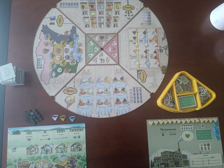 Fromage game board fully set up with all four venues, the central resource tile, a player board, order card deck, resource tray, and the Corporation's level 4 solo board laid out on the table