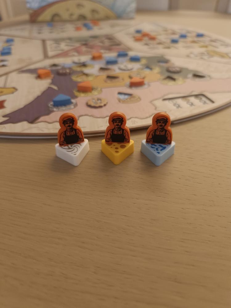 Three Fromage worker meeples on soft, hard, and bleu cheese worker bases standing in front of the game board