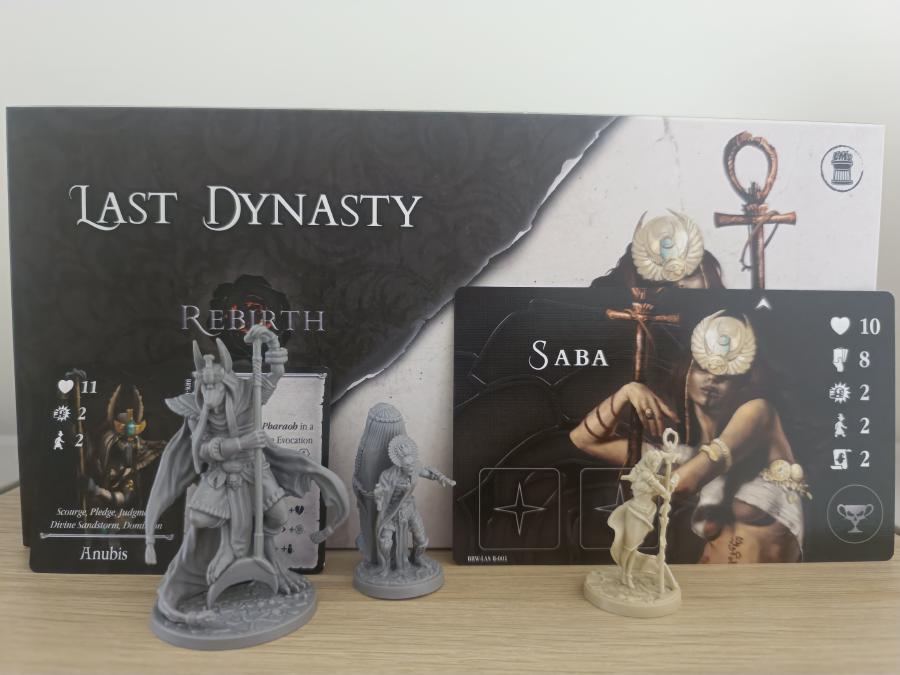 Last Dynasty box from the Rotas Box with the Anubis avatar card and miniature on the left and the Saba mage board and miniature on the right