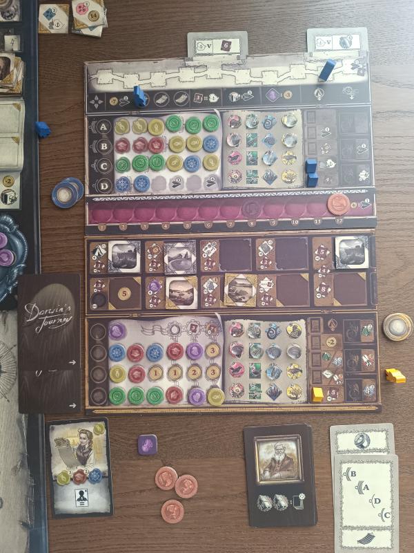 Close-up of a Darwin's Journey player board covered in coloured wax seal tokens, with specimen tiles, coins and cards around it
